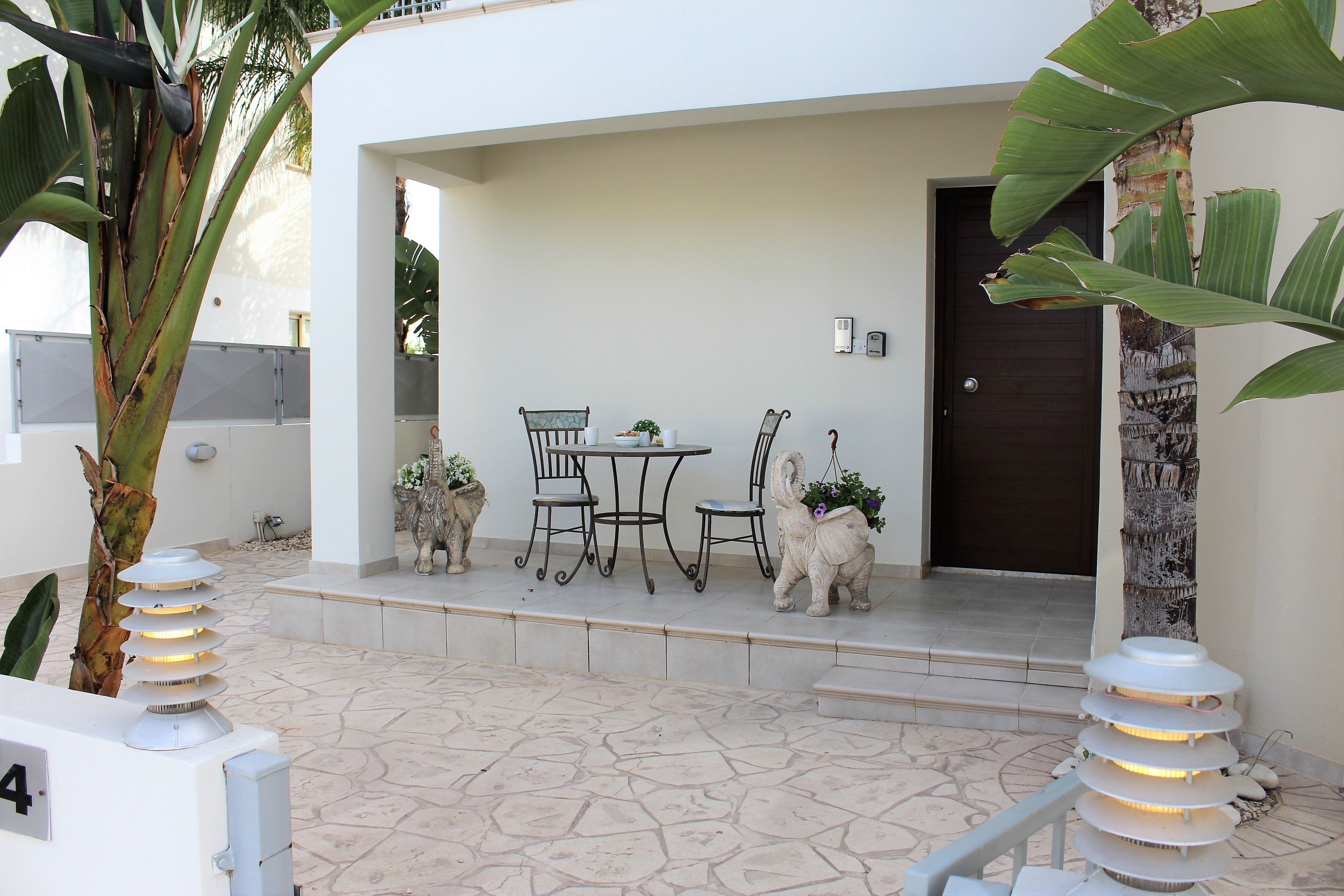 A patio with a table and chairs, a door, and decorative plants.