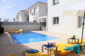 A swimming pool with yellow lounge chairs and a table with drinks and snacks. - Avrora Villa PV (Paralimni)