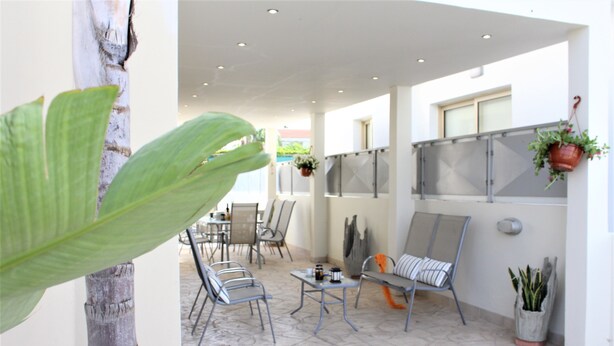 Un amplio patio con sillas y mesas de metal, una gran maceta y jardineras colgantes.