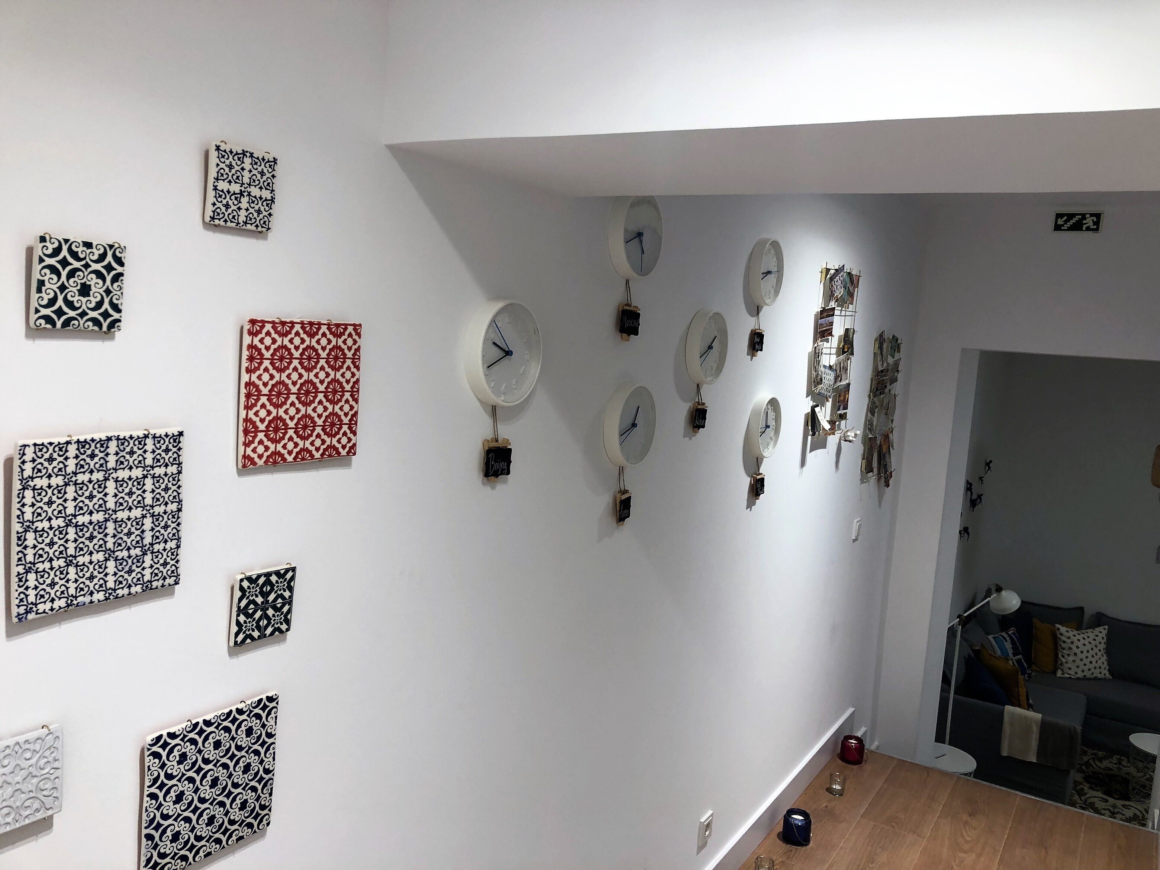 A room with a white wall displaying various patterned tiles and multiple clocks.