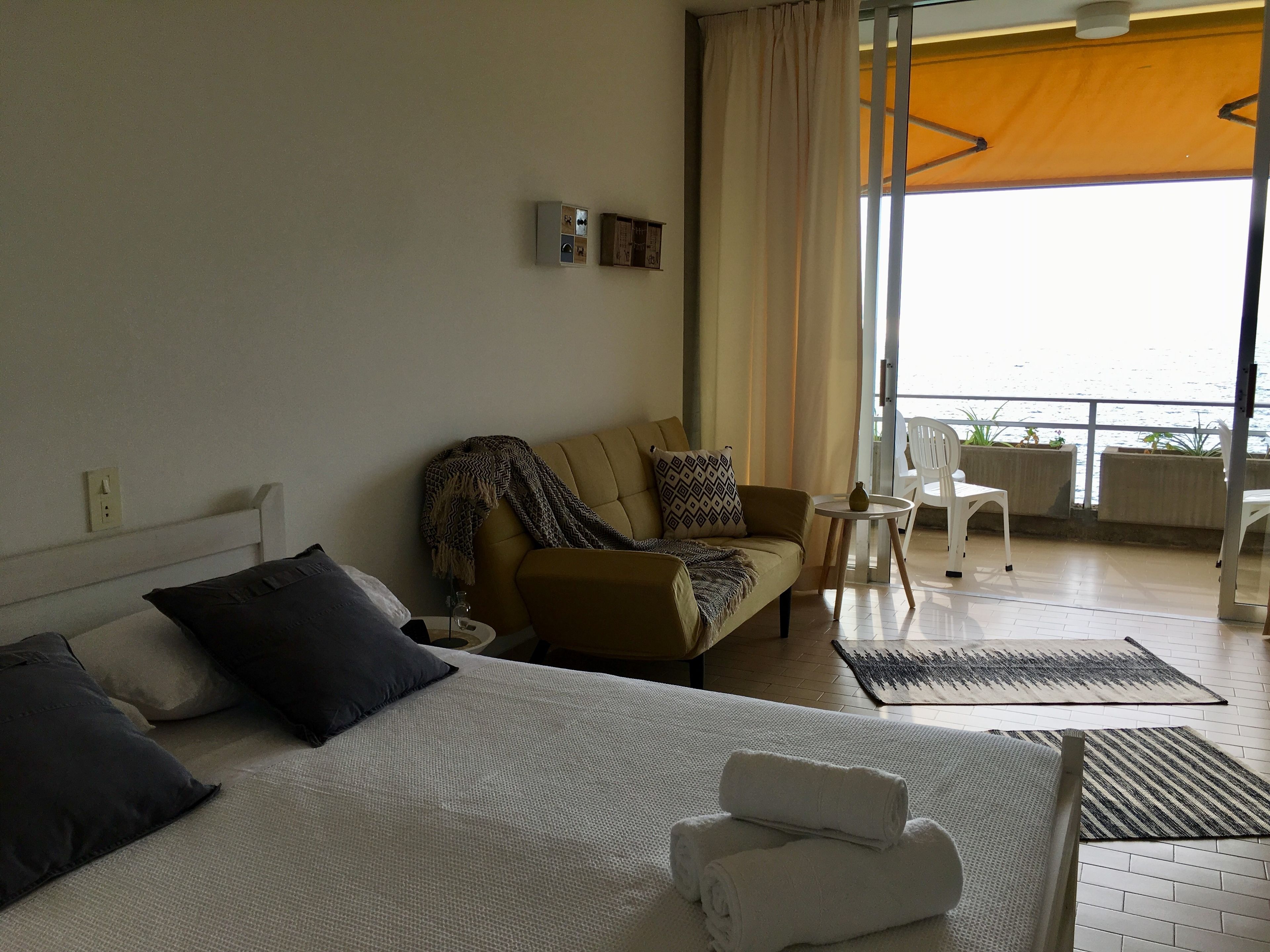 A hotel room with a bed, a sofa, a small table with a vase, and a view of the sea through large windows.