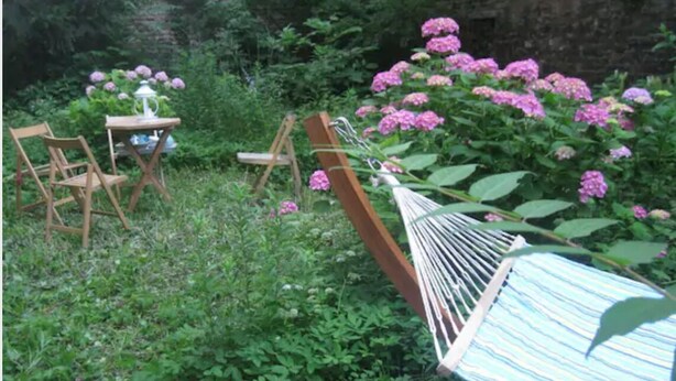 A garden with a wooden bench, a table with chairs, and pink flowers. - Apartment Mariahilf (Vienna)