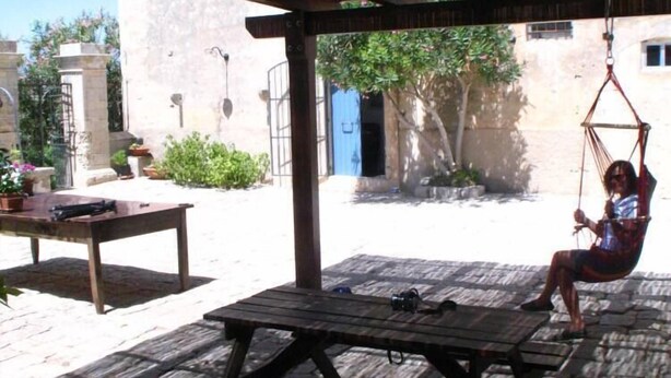 A covered outdoor seating area with a swing, a picnic table, and a view of a building in the background. - A holiday home in the Iblea countryside a stone's throw from the sea (Ragusa)