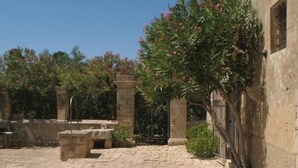 A courtyard with stone paving, a fountain, and a building with a gate. - A holiday home in the Iblea countryside a stone's throw from the sea (Ragusa)
