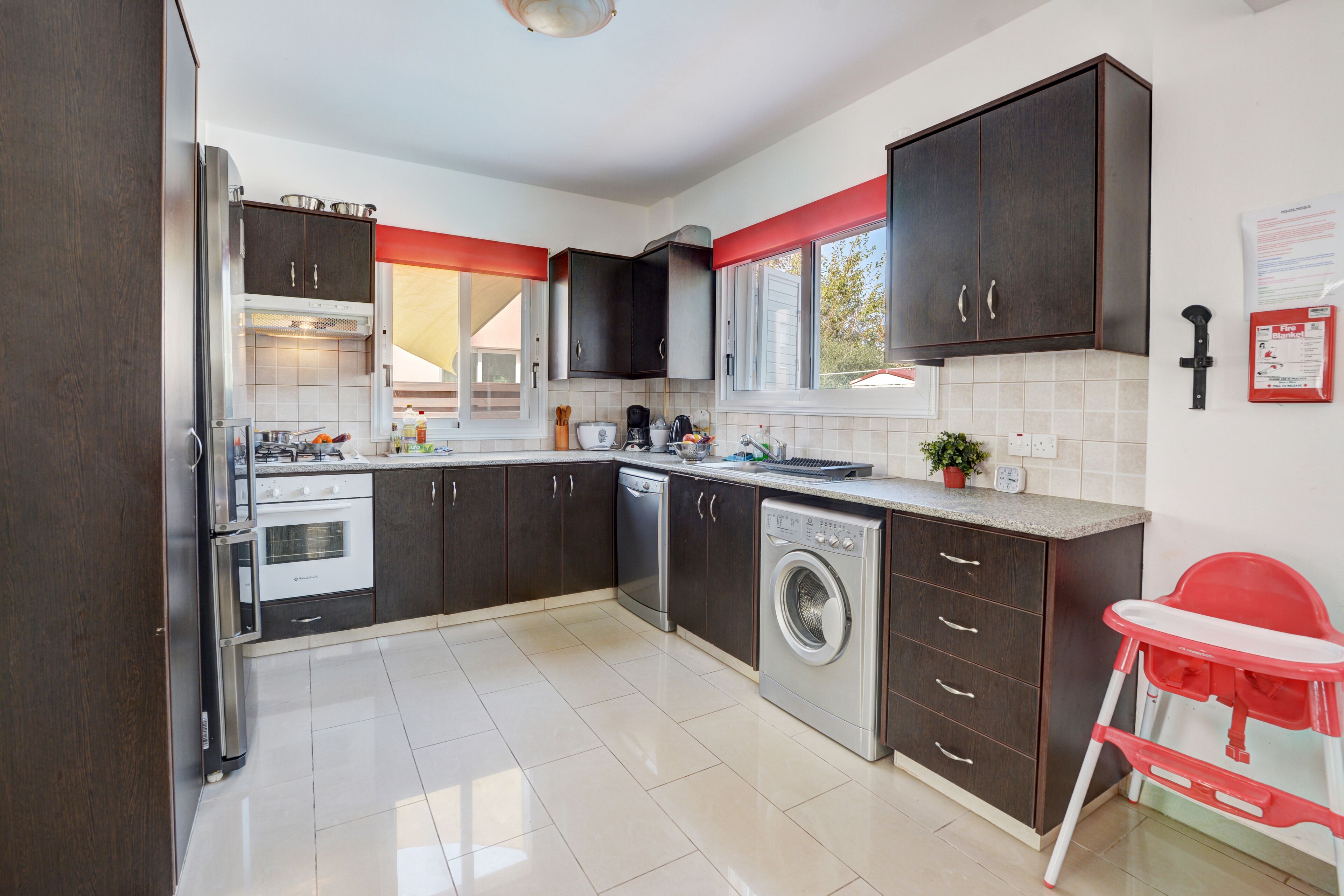 A modern kitchen with dark cabinets, stainless steel appliances, and a red and white high chair.
