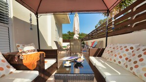 Un espace extérieur aménagé avec des meubles en osier, une table à plateau en verre et un patio couvert.