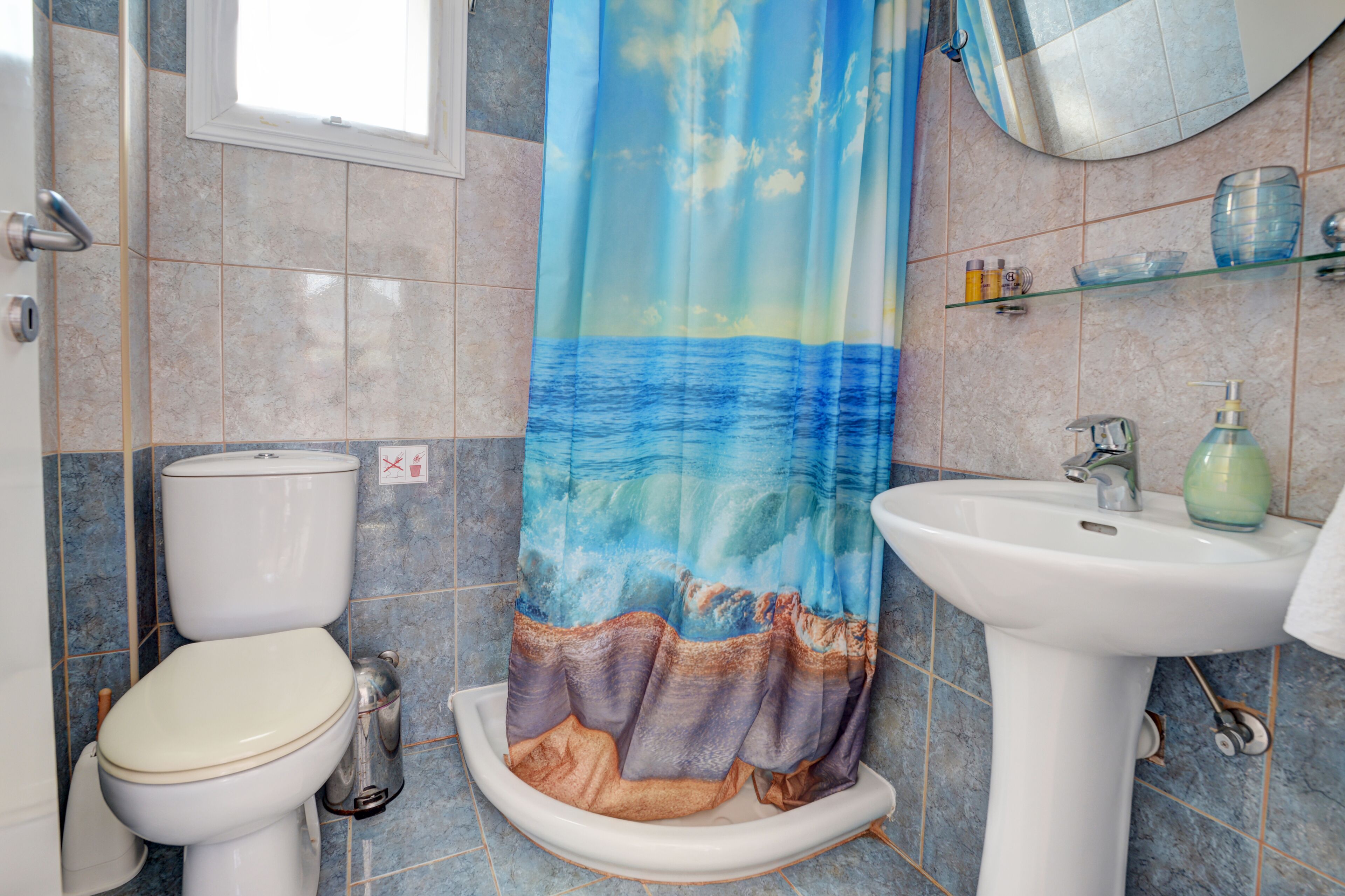 A bathroom with a toilet, sink, and shower curtain depicting a seascape.