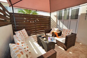 A patio area with wicker furniture, a glass coffee table, and a wooden fence.