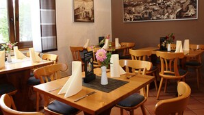 Un restaurante con mesas y sillas de madera, una fotografía grande en blanco y negro en la pared, y un atril para el menú con un florero.