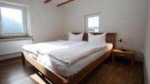 Un dormitorio con una cama de madera, dos ventanas, una mesita de noche y un radiador.