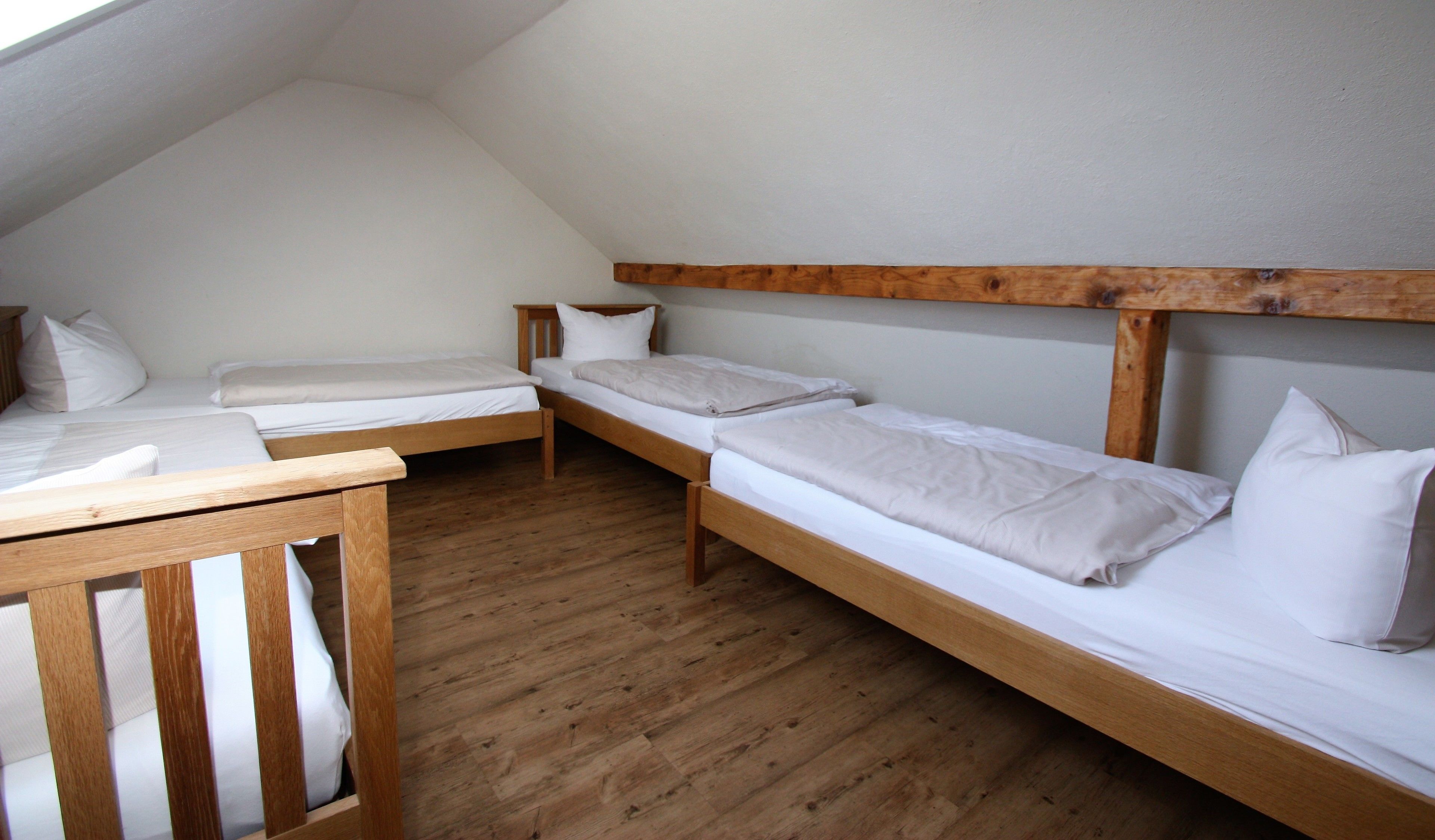A dormitory room with three wooden bunk beds, white bedding, and a wooden table.