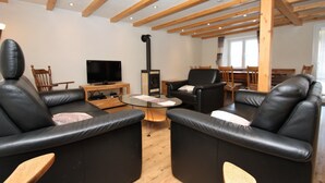 Una sala de estar moderna con sofás de cuero negro, una mesa de centro de vidrio, vigas de madera en el techo, un televisor y una chimenea.