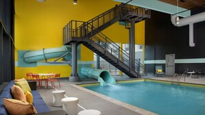 An indoor swimming pool with a slide, a staircase, and seating areas.