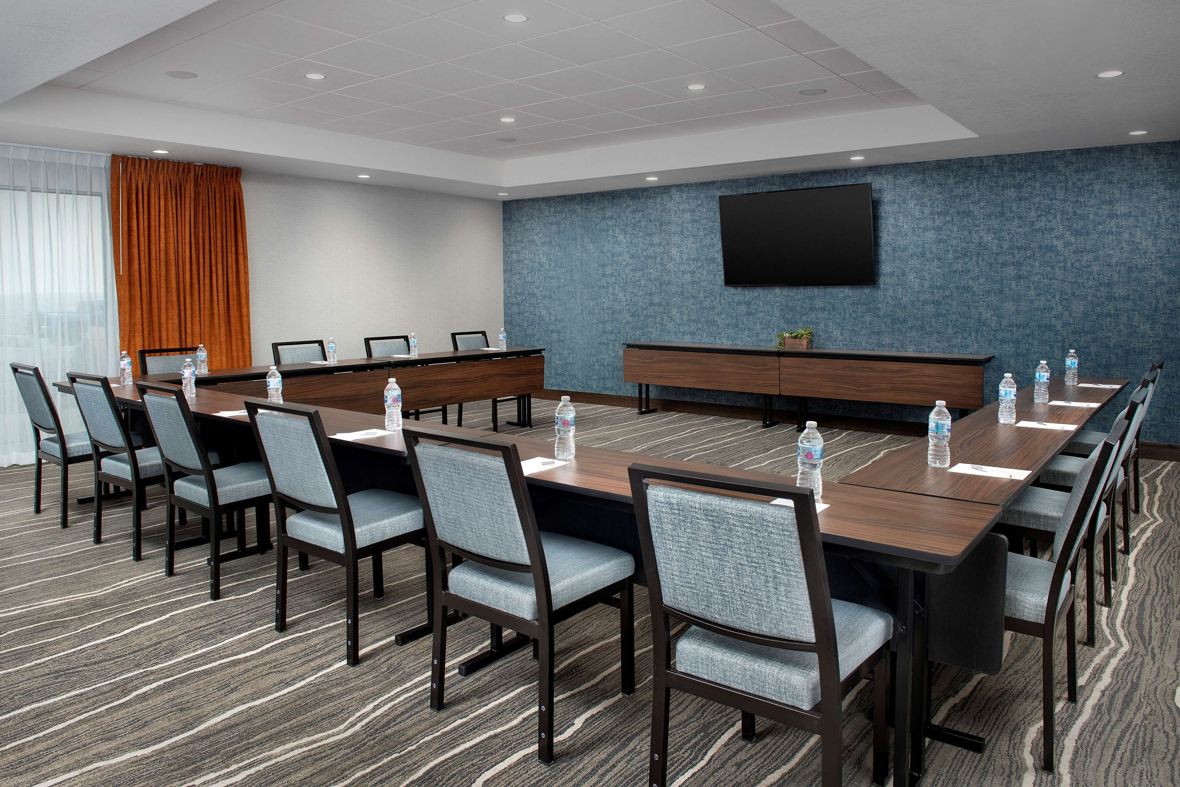 A conference room with a long table, chairs, water bottles, a TV screen, and a blue textured wall.