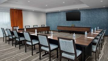 A conference room with a long table, chairs, water bottles, a TV screen, and a blue textured wall.