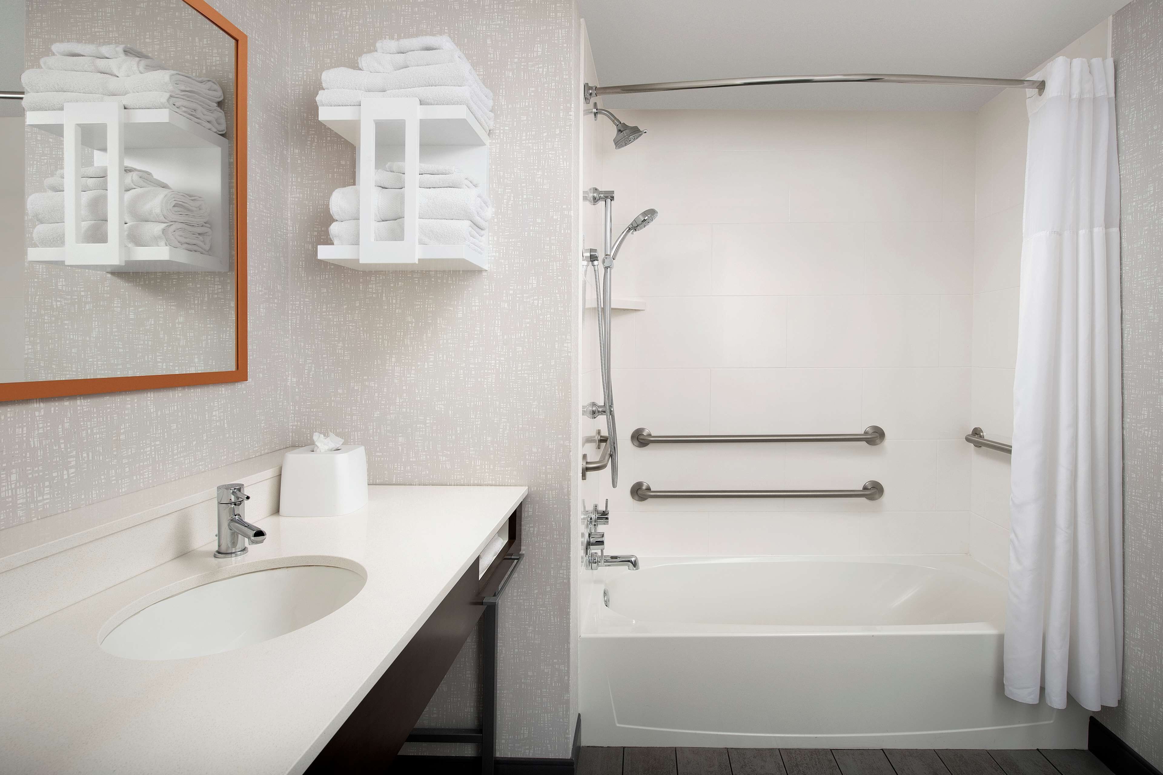 A modern bathroom with a sink, mirror, towel racks, and a walk-in shower with grab bars.