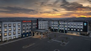 A hotel with a parking lot, a gas station, and a view of mountains during sunset.