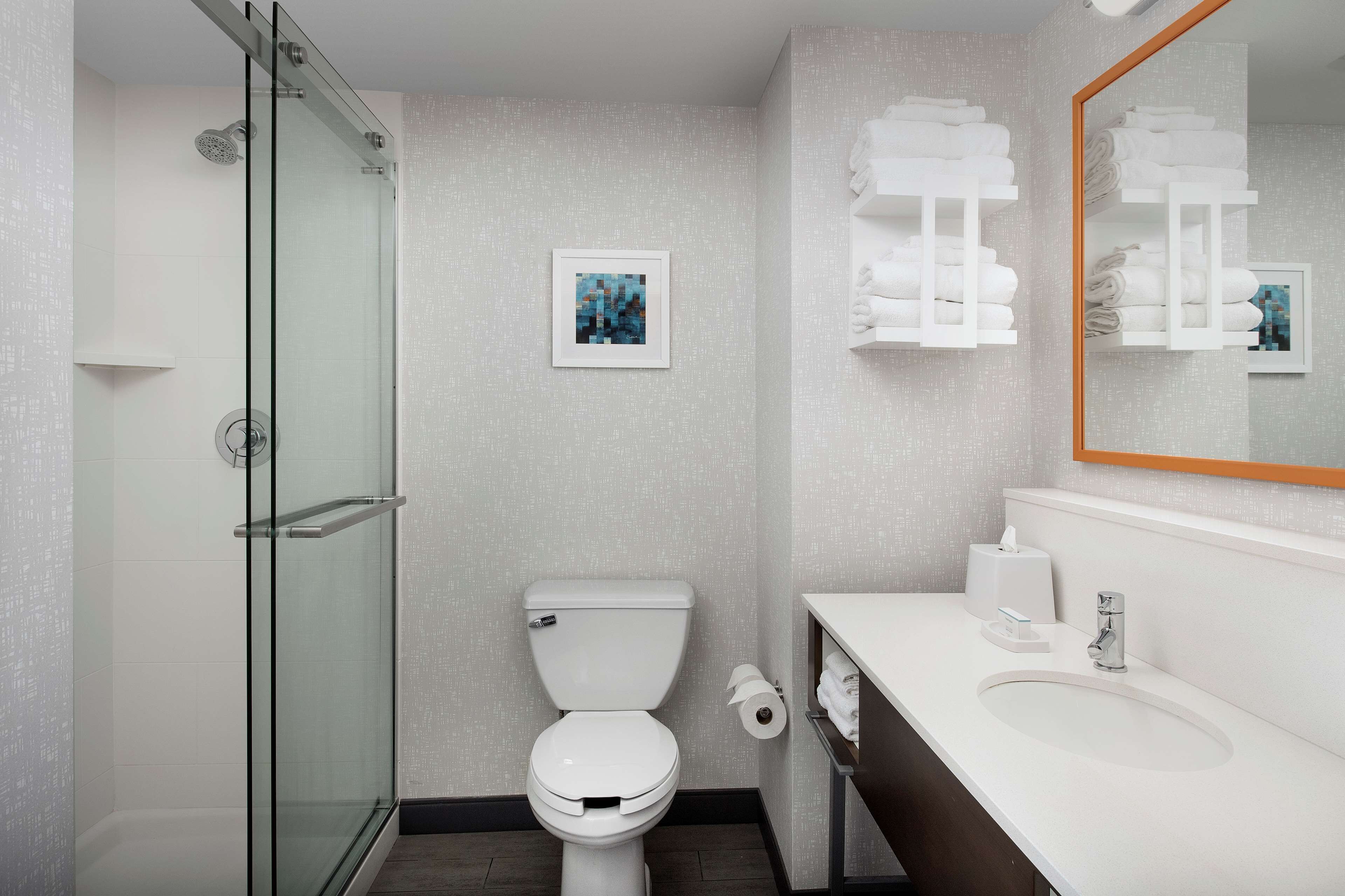 Un baño moderno con cabina de ducha de vidrio, inodoro, lavabo con espejo y toalleros.