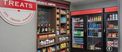 A treats section in a store with shelves of snacks and a refrigerated display with beverages.