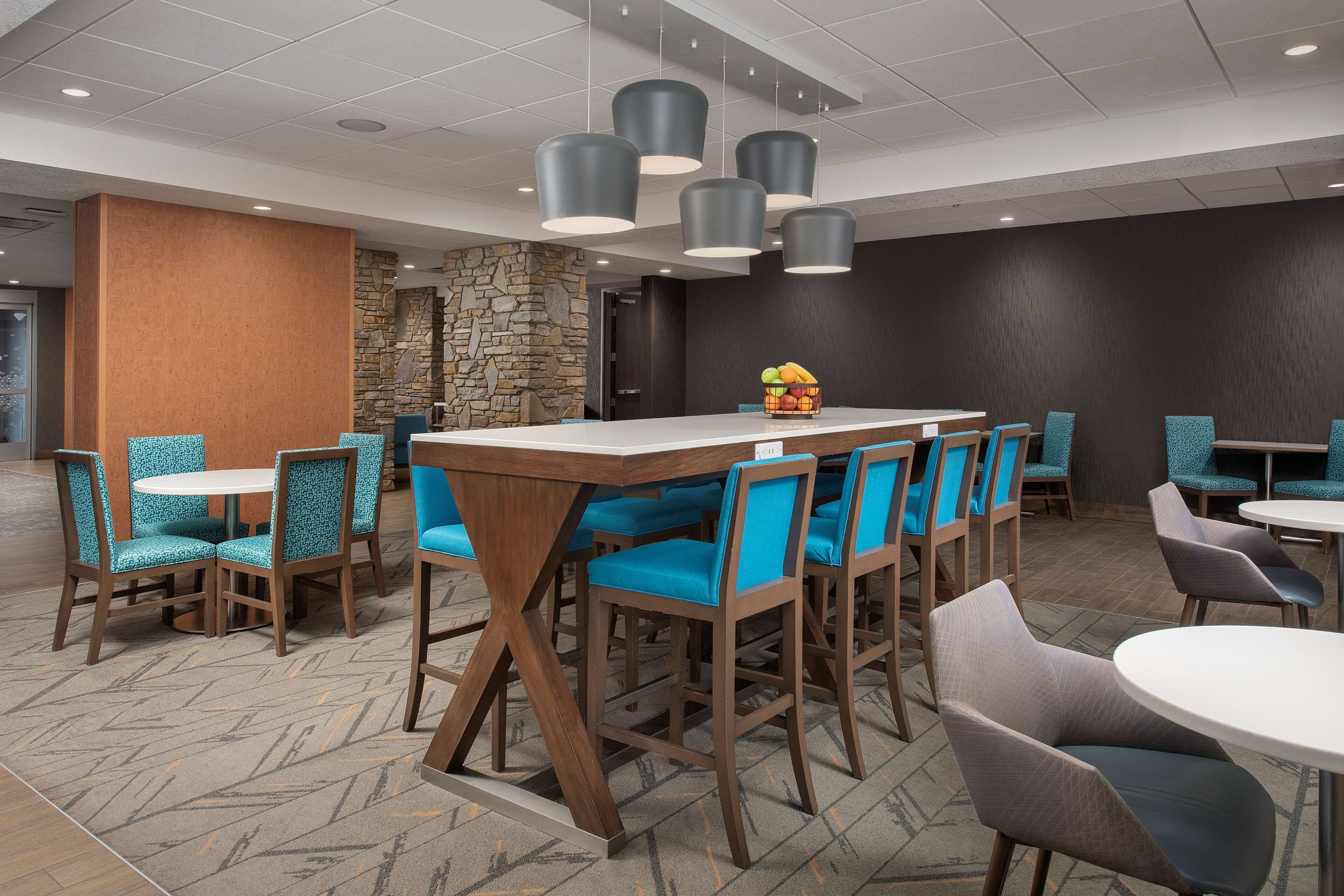 A modern dining area with round tables and blue upholstered chairs, featuring a stone accent wall and overhead pendant lighting.