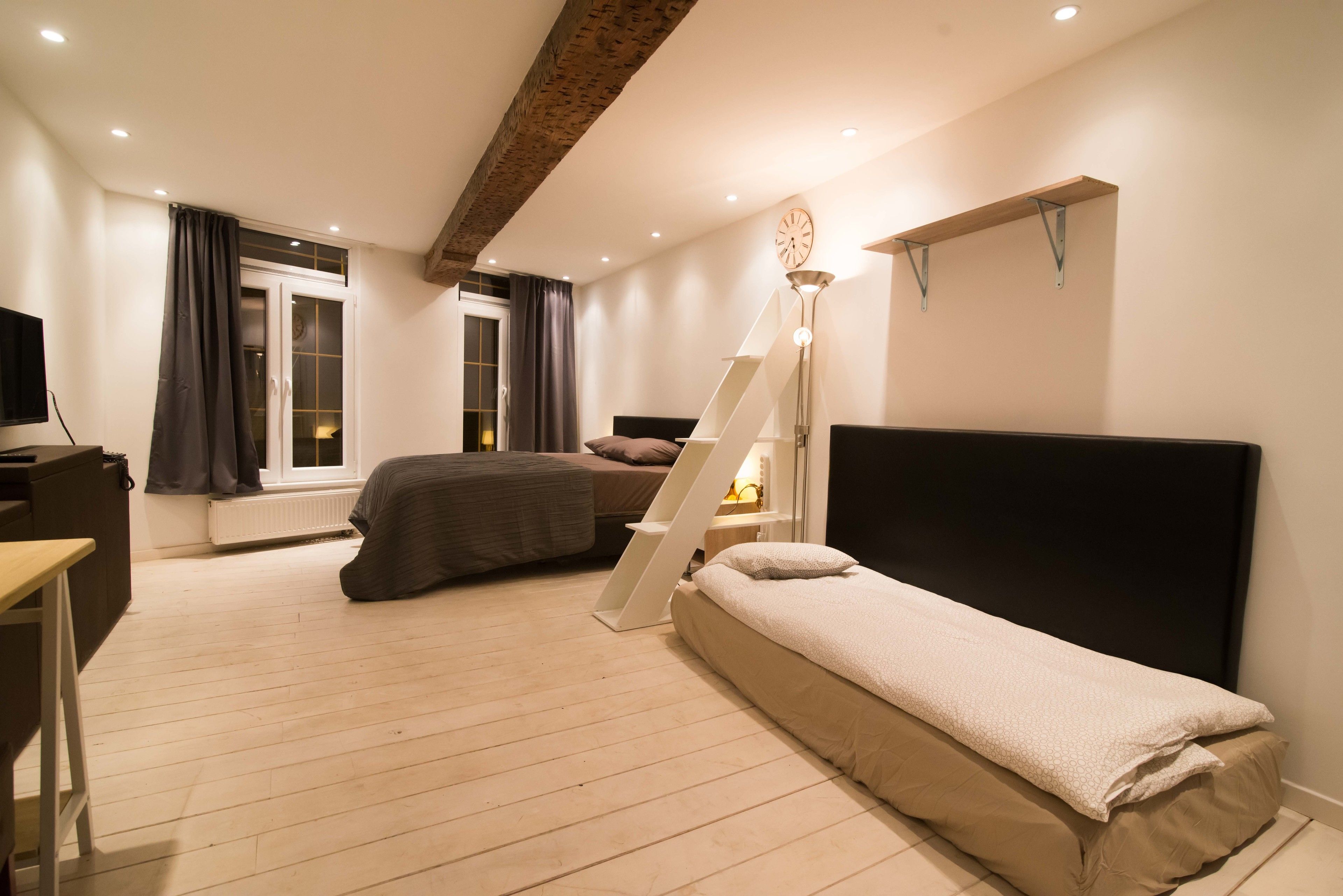 Un dormitorio con cama, escritorio, silla, escalera y televisor.