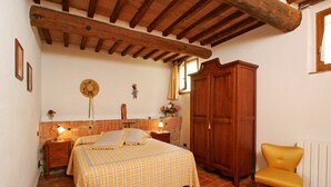 Une chambre à coucher comprenant un lit, une tête de lit en bois, des tables de chevet, une armoire, une chaise et une fenêtre avec des rideaux.