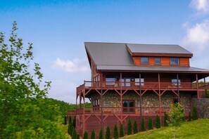 A two-story log cabin with a stone foundation, a balcony, and a sloped roof.