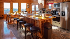 A wooden cabin kitchen with a bar area, bar stools, a refrigerator, and a view through the windows.