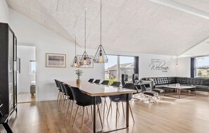 A spacious dining area with a long wooden table, black chairs, and pendant lights. There is a black leather sofa and a small table with a vase of flowers. - Awesome home in Haderslev with WiFi (Haderslev)