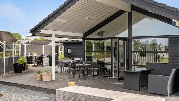 A covered outdoor patio with a dining area, including tables and chairs, and a grill.