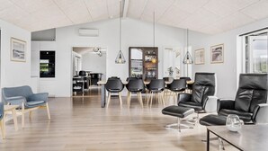 A spacious living area with a high ceiling, a dining area with black chairs and a wooden table, and a seating area with leather chairs and ottomans.
