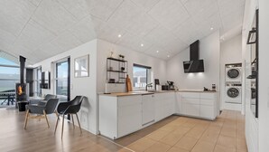 A modern kitchen with white cabinetry, a built-in stove, and a dining area with a view.