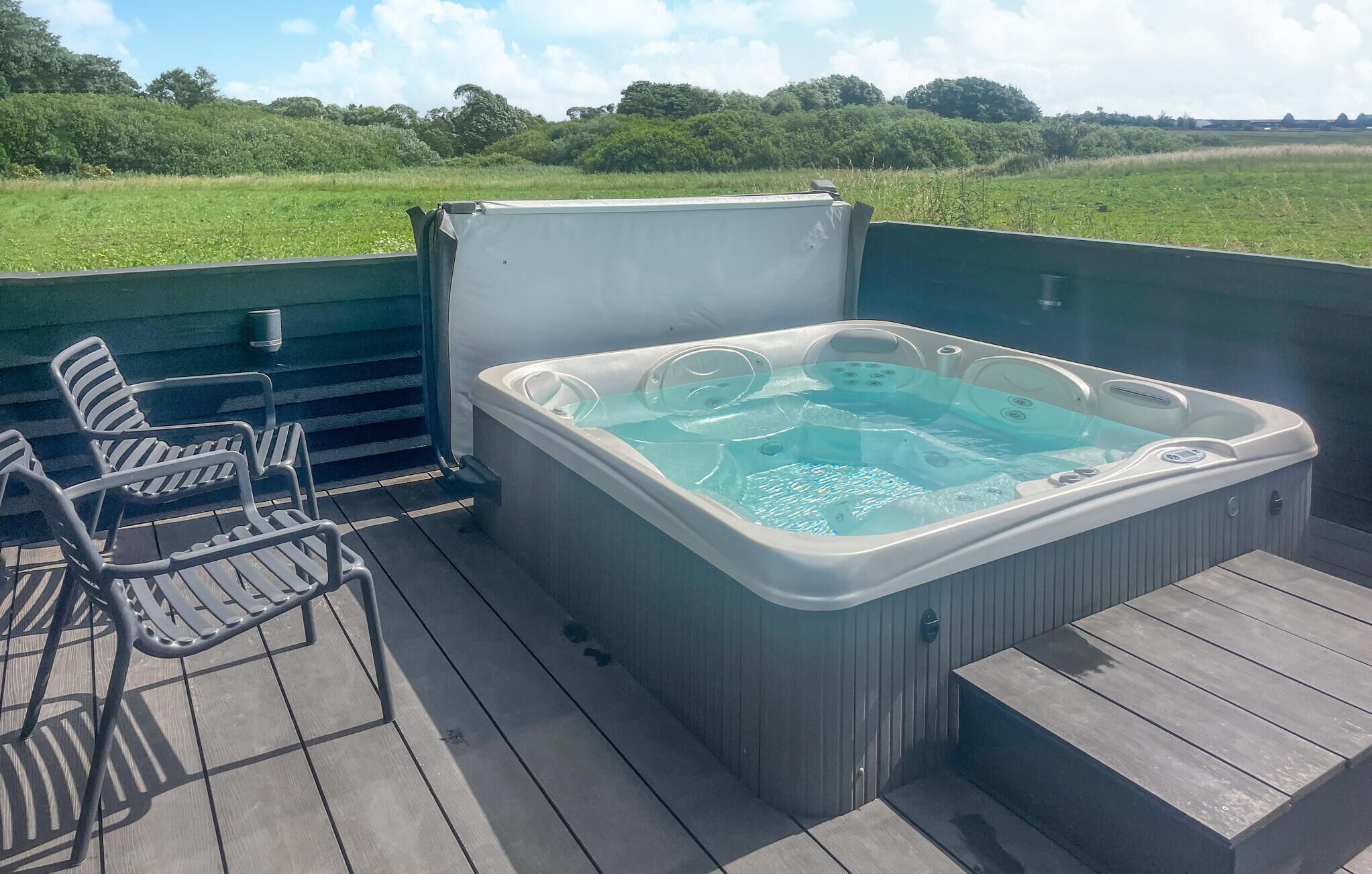 Ein Whirlpool auf einer Terrasse im Freien mit Stühlen und Blick auf ein grünes Feld.