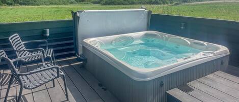 Ein Whirlpool auf einer Terrasse im Freien mit Stühlen und Blick auf ein grünes Feld.
