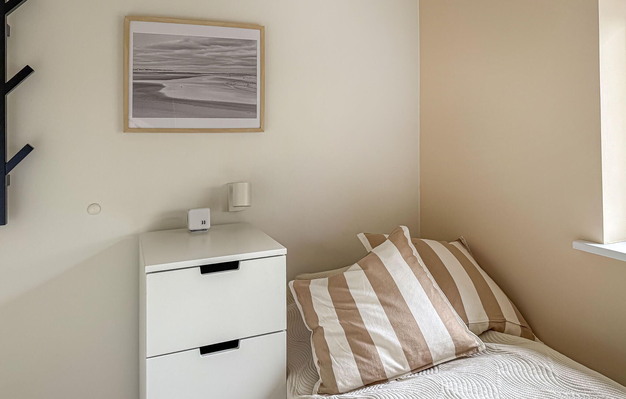 Une chambre à coucher avec un lit, une table de chevet avec une lampe, un tableau accroché au mur et une commode blanche.