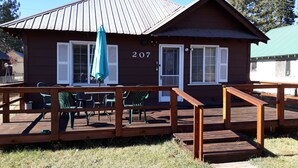 A wooden cabin with a number 207, a deck with chairs, and a covered patio area.