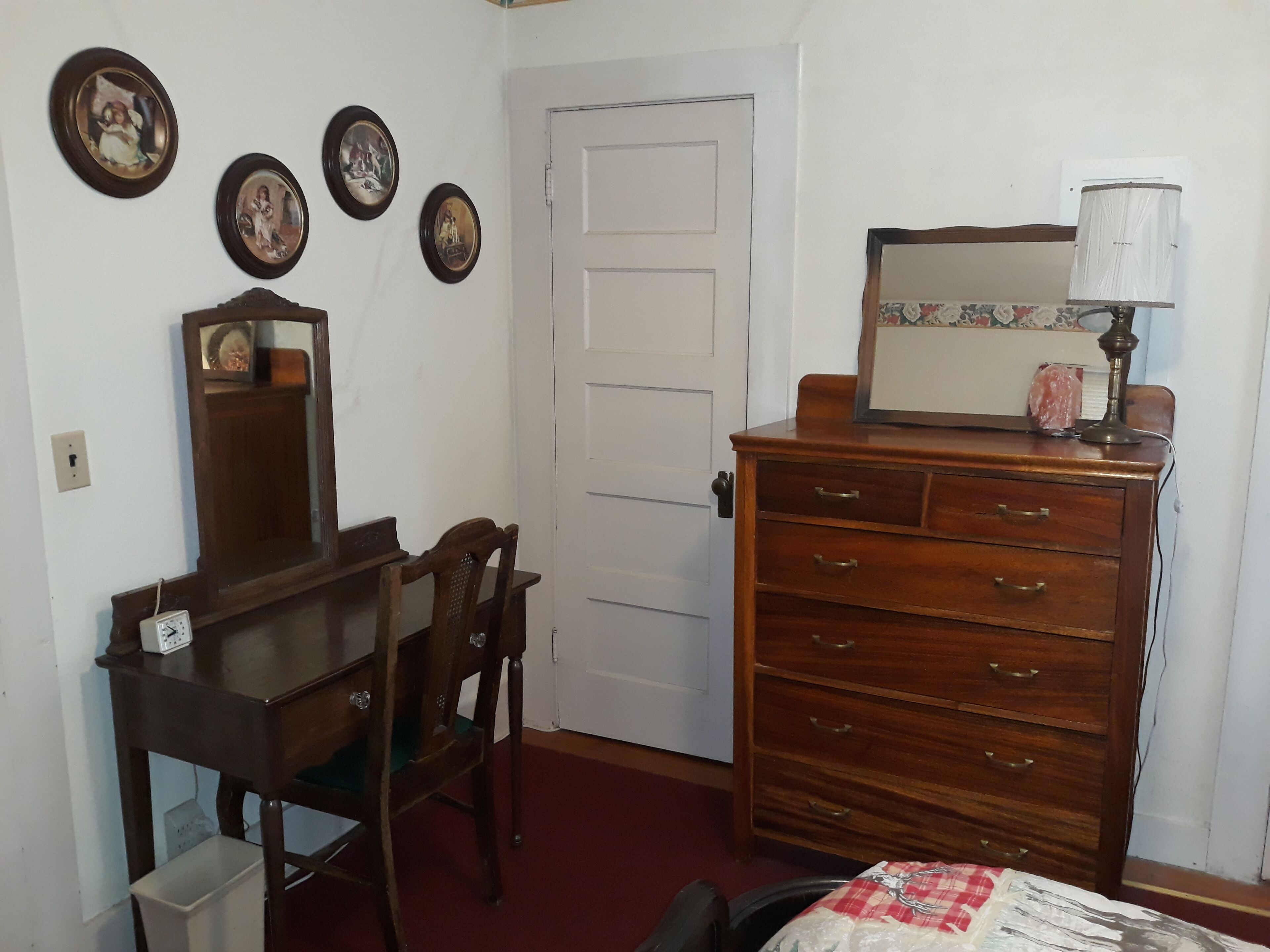 Una habitación con un aparador de madera, un espejo y una mesa con sillas. Cuatro cuadros enmarcados adornan la pared.