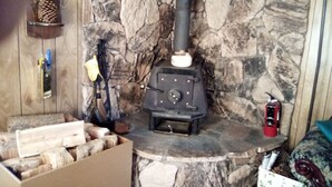 A rustic stone wall with a wood-burning stove labeled "ROUGH ROAD" and a box of firewood.