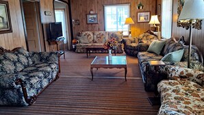 A cozy living room with floral-patterned sofas, a wooden floor, a coffee table with a vase of flowers, and a television.