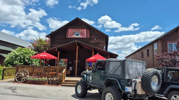 A rustic building with a sign for Buffalo Chip's Pizza & Pub, a Jeep parked in front, and a wooden fence with a flower bed.
