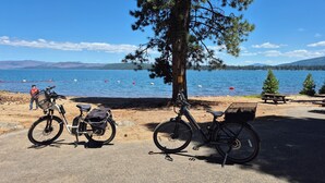 Un entorno junto al lago con bicicletas estacionadas cerca de una mesa de picnic y una persona al fondo.