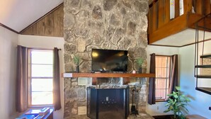 A stone fireplace with a television above it, a wooden bench, and a potted plant. - Fantastic Pool, Hot Tub, Cabana, Mt. Views, Party Pavilion, 2 Minutes 2 Frio! (Concan)