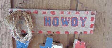 A wooden sign with the word "HOWDY" in red and blue letters, a blue Texas flag, and a red and white cowboy hat.
