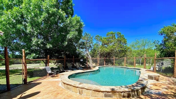 A swimming pool with a stone edge, surrounded by a wooden fence and chairs. - Fantastic Pool, Hot Tub, Cabana, Mt. Views, Party Pavilion, 2 Minutes 2 Frio! (Concan)