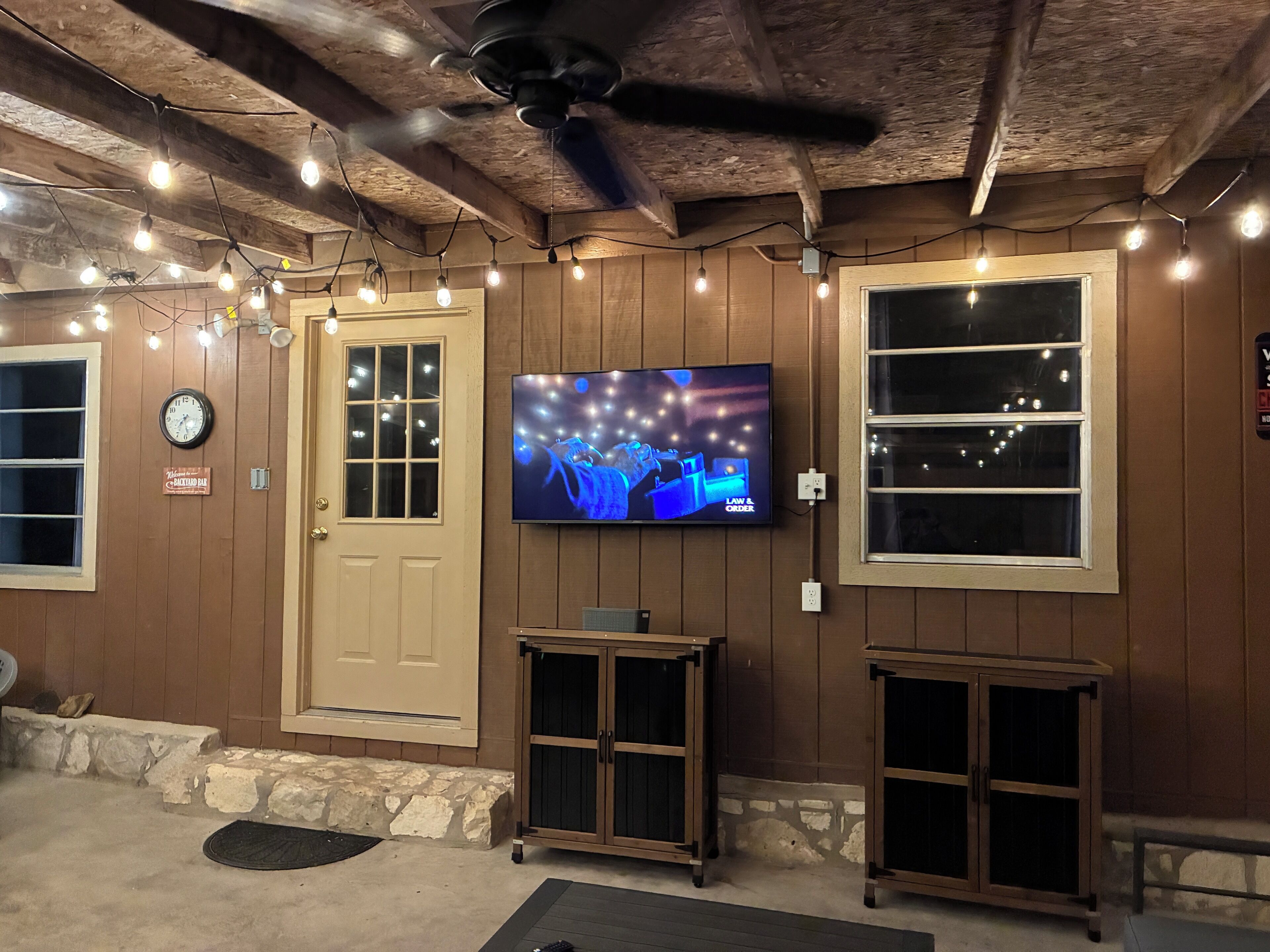A room with wooden walls, a ceiling fan, a TV mounted on the wall, and a door with a window.