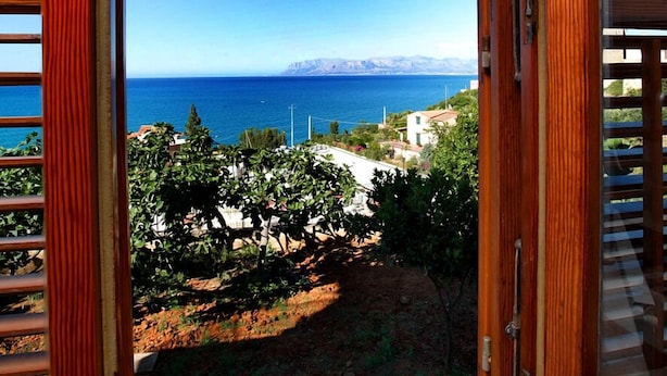 Une porte en bois donnant sur un balcon avec vue sur la mer et les montagnes.