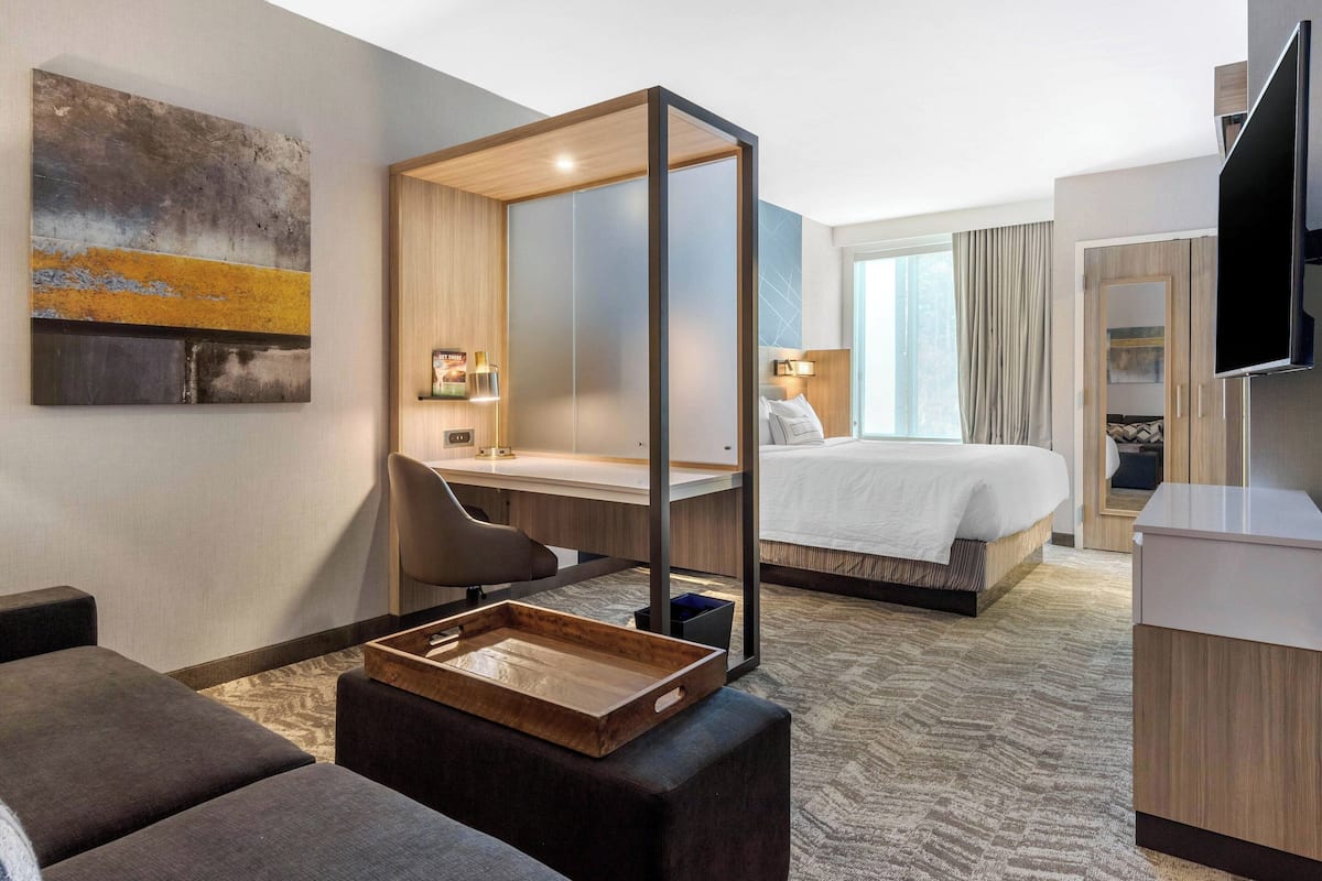 Habitación de hotel con cama, escritorio, silla, televisor y un ventanal grande.