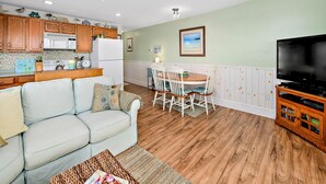 Uma sala de estar com um sofá, uma mesa de jantar com cadeiras, uma televisão e armários de madeira.
