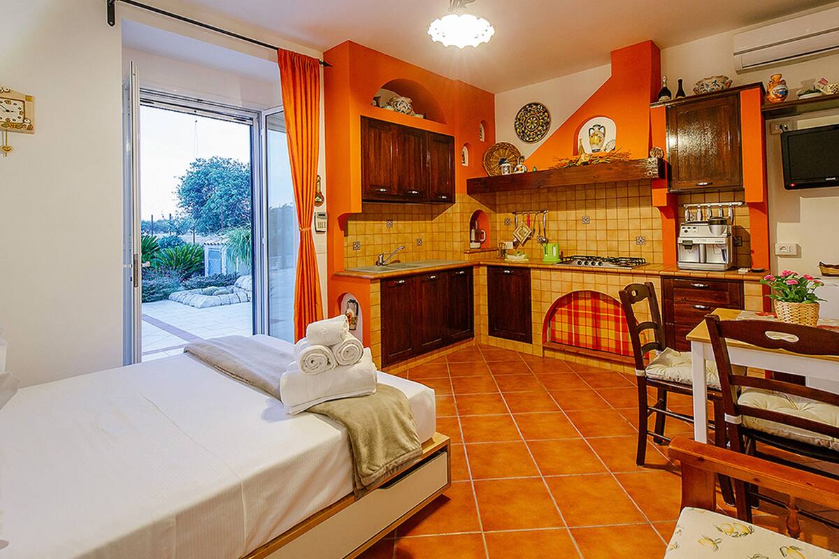 A bedroom with a bed, a bathroom with a shower, and a kitchen with a stove and sink.