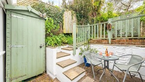 A patio with a table and chairs, a green gate, and a white wall with steps leading up to a wooden deck.